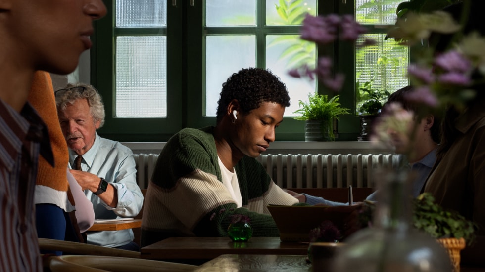 Person trägt AirPods 5 in einem belebten Café – offizielles Apple-Newsroom-Foto