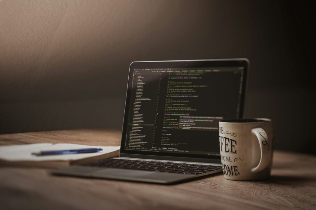 Laptop mit Code-Editor auf einem Holztisch neben einer Kaffeetasse